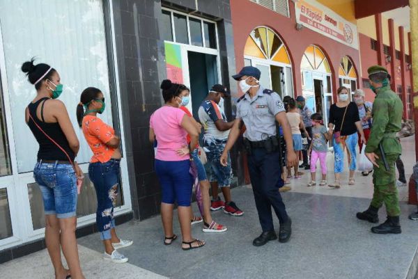 police officers watch the discipline of people who are standing in line outside a cafeteria in sancti spiritus, cuba